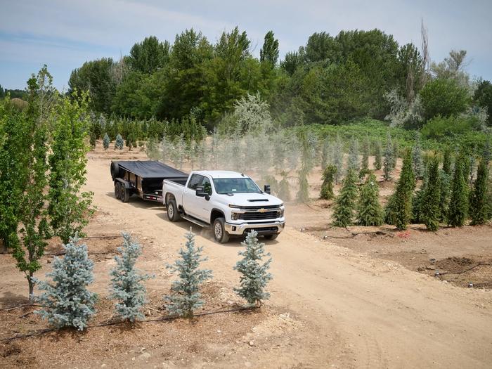 White truck towing a dump trailer on a dirt road through green trees