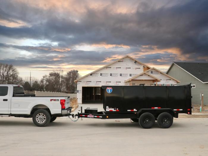 Charcoal-gray Interstate enclosed cargo trailer with diamond-plate stone guard parked on asphalt next to a grassy roadside