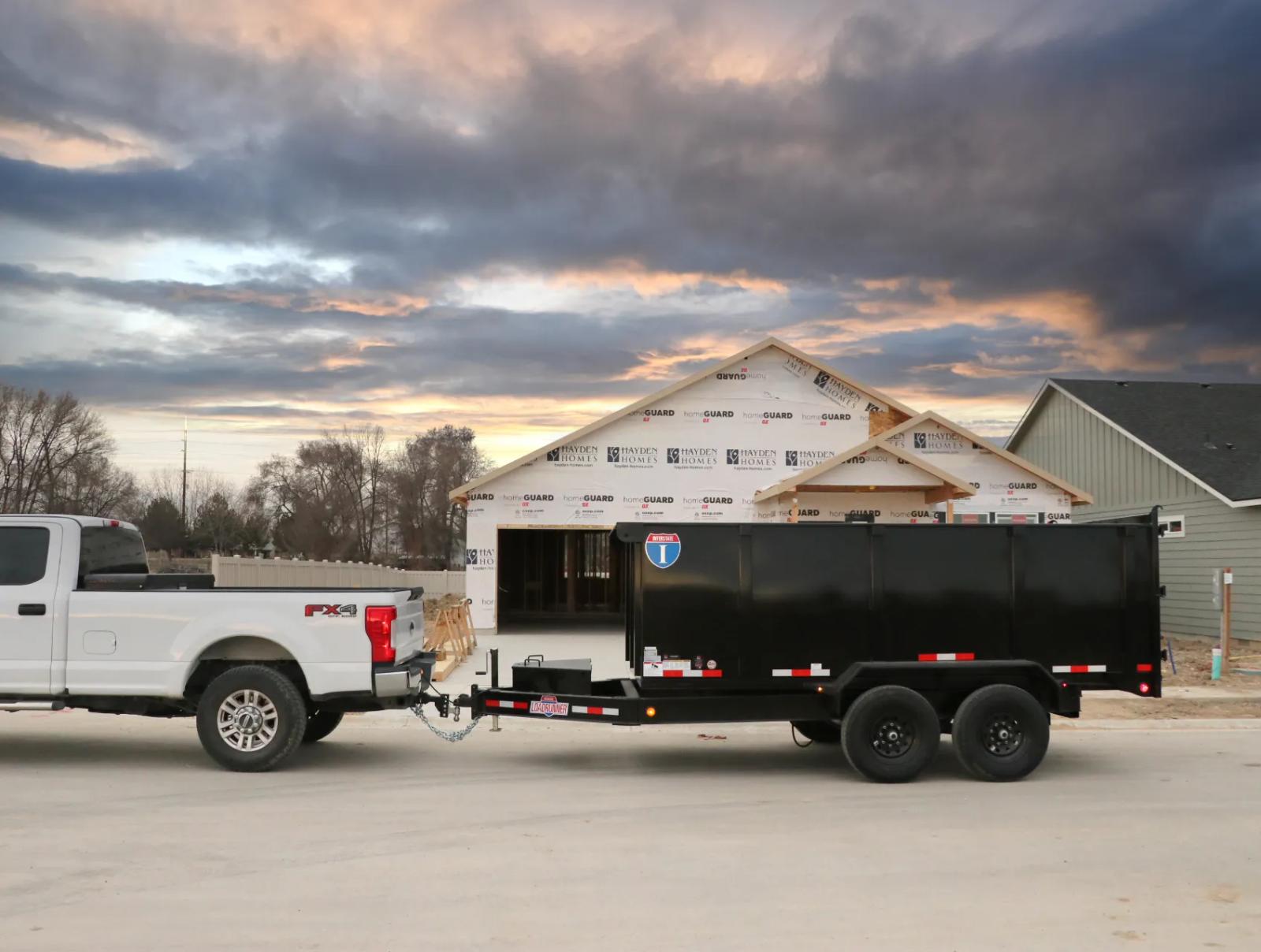 Charcoal-gray Interstate enclosed cargo trailer with diamond-plate stone guard parked on asphalt next to a grassy roadside