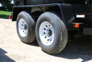 Close-up of a black trailer's tandem axles with silver wheels and a silver diamond-plate fender