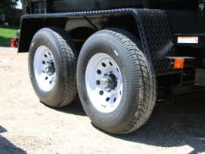 Close-up of a black trailer's tandem axles with silver wheels and a silver diamond-plate fender