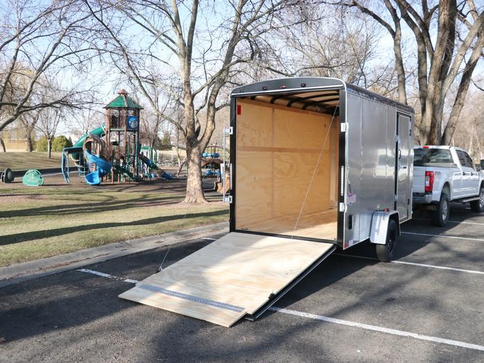 Charcoal Interstate enclosed cargo trailer with rear ramp deployed in a paved lot beside a children's playground and bare trees