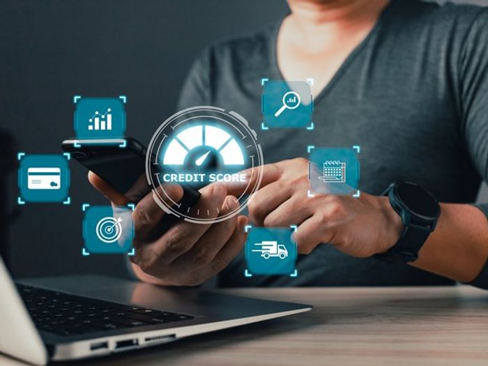 Stock photo of a person holding a smartphone with a glowing 'Credit Score' meter graphic and finance icons floating around it