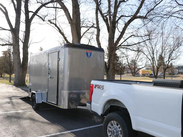 Charcoal Interstate enclosed cargo trailer hitched behind a white pickup truck parked under bare trees in a paved lot