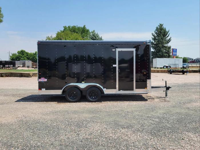 Black tandem-axle dump trailer with the bed raised in dump position, parked on a sunny TrailersPlus lot near rows of cargo trailers