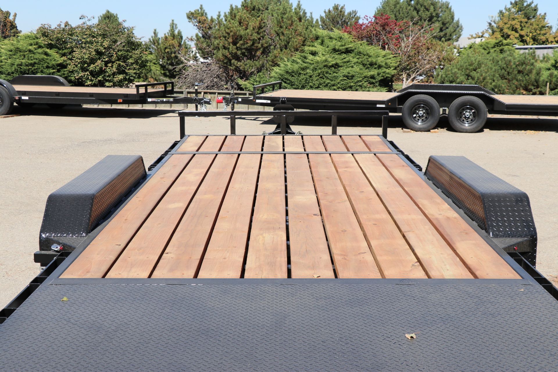 Low-angle view of a black utility trailer's commercial-strength hardwood plank deck and black diamond-plate fender