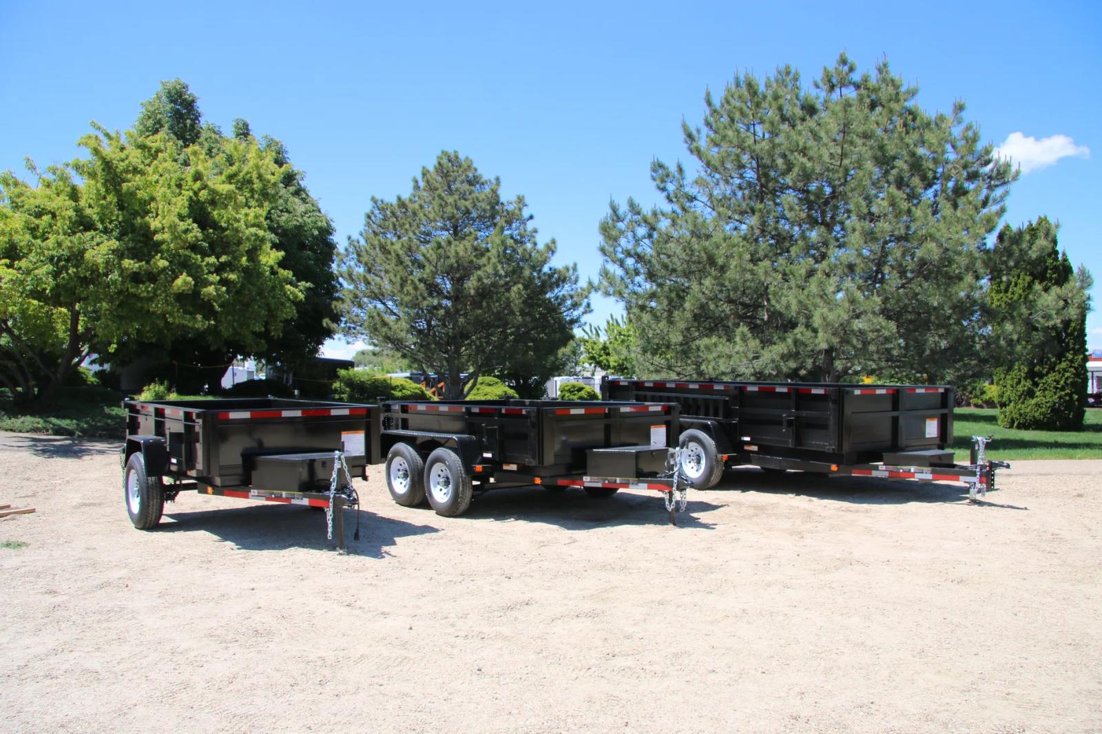 Three black dump trailers of varying sizes parked side-by-side on a sandy dealer lot under a clear sky