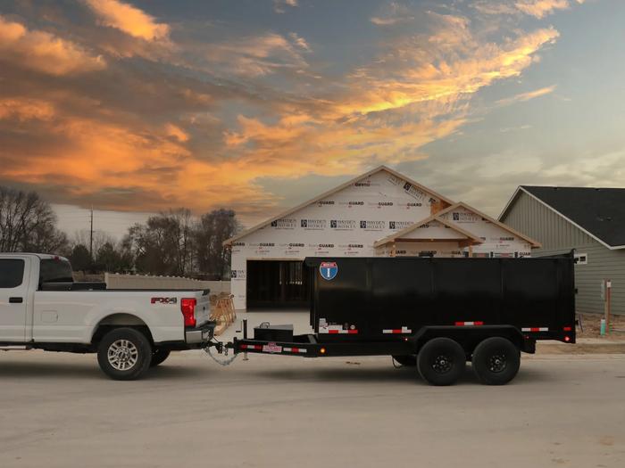 Charcoal-gray Interstate enclosed cargo trailer with diamond-plate stone guard parked on asphalt with a covered shed in the background