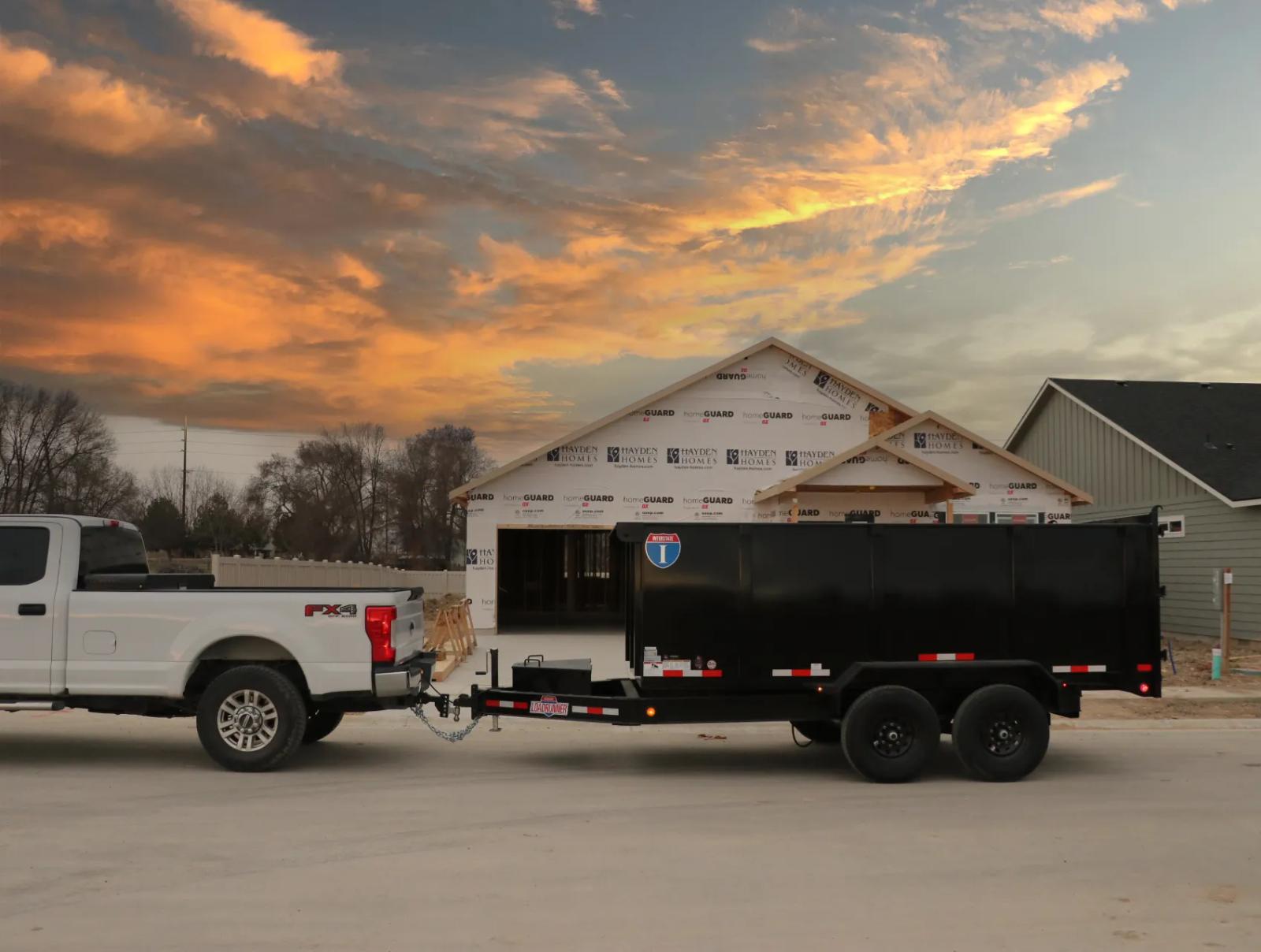 Charcoal-gray Interstate enclosed cargo trailer with diamond-plate stone guard parked on asphalt with a covered shed in the background