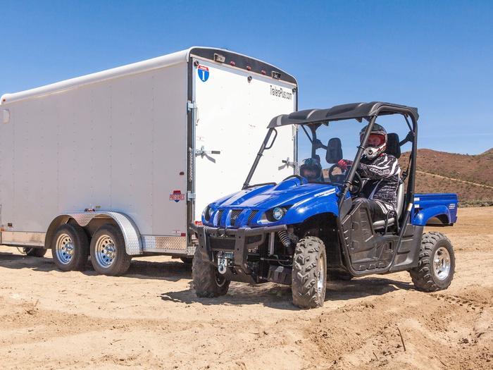 White enclosed cargo trailer hooked behind a pickup with a blue Yamaha UTV parked next to it on a desert dirt lot