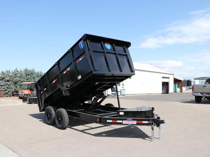 Black dump trailer with tall side extensions and the bed tilted up at full angle, parked at a warehouse with a forklift in the background