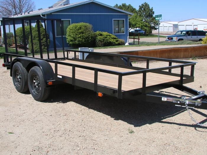 Lineup of a black utility trailer, flatbed deckover, gooseneck dump, and enclosed cargo trailers parked together on a TrailersPlus dealer lot under cloudy skies