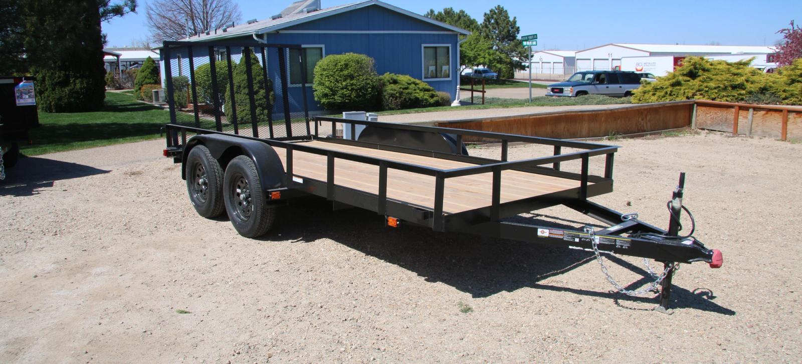 Utility trailer with wood decking on a dirt ground with a blue building in the background