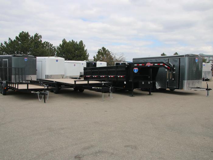 Lineup of a black utility trailer, flatbed deckover, gooseneck dump, and charcoal enclosed cargo trailers parked at a TrailersPlus lot