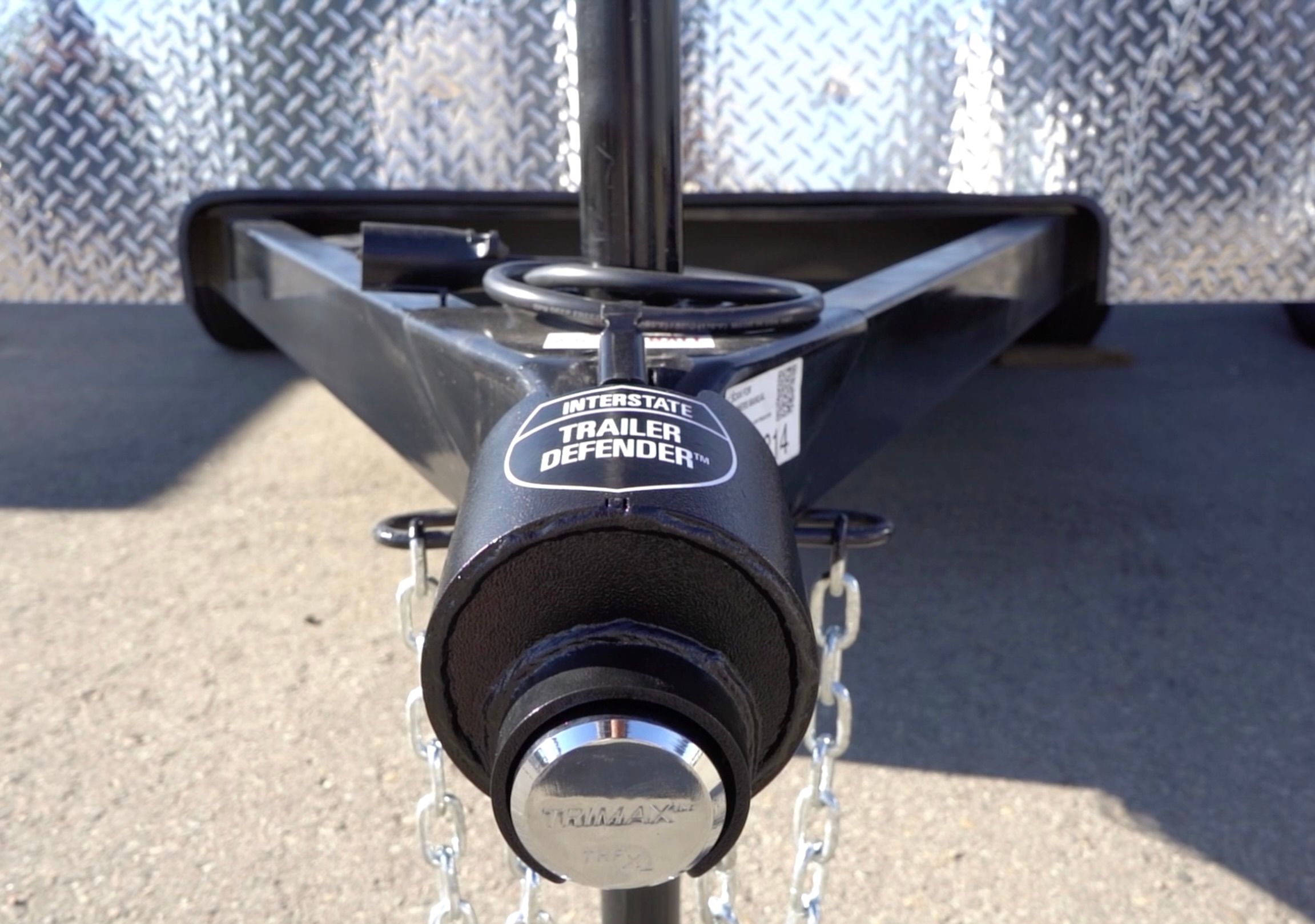 Close-up of a black trailer tongue with an Interstate Trailer Defender coupler lock and safety chains attached