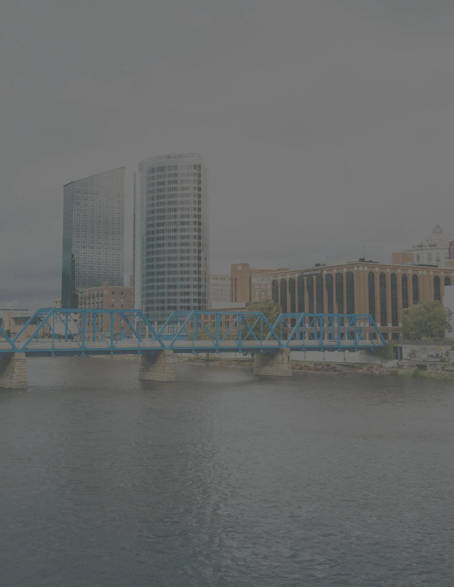 Faded skyline view of Grand Rapids' blue truss pedestrian bridge and downtown high-rises across the river