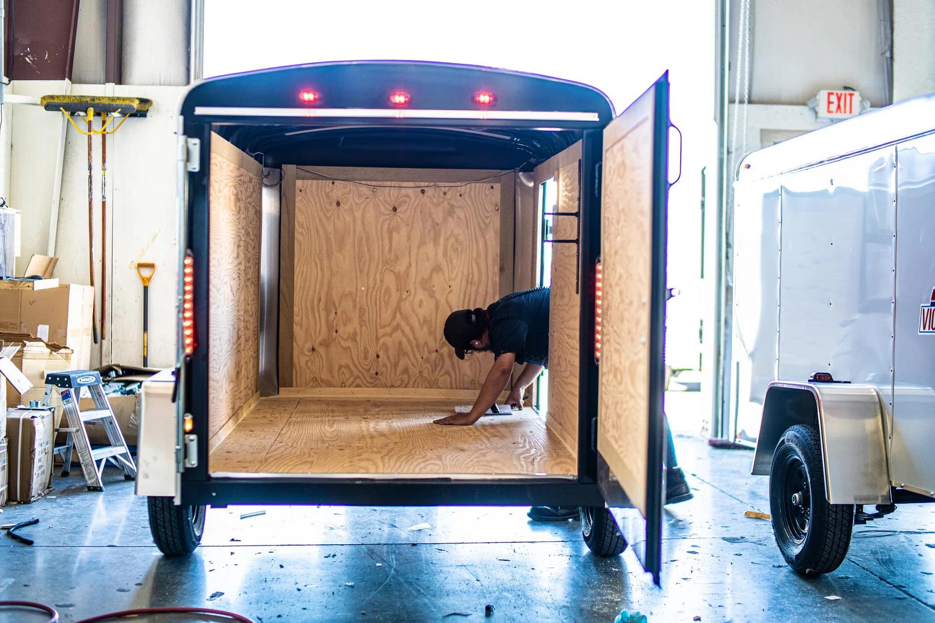 Charcoal Interstate enclosed cargo trailer parked at a residential framing site with workers and ladders at a half-built two-story home