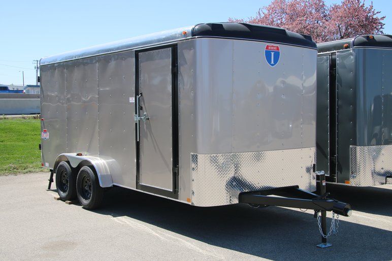 Rows of black single-axle utility trailers with wood decks lined up at a sunny TrailersPlus dealer lot