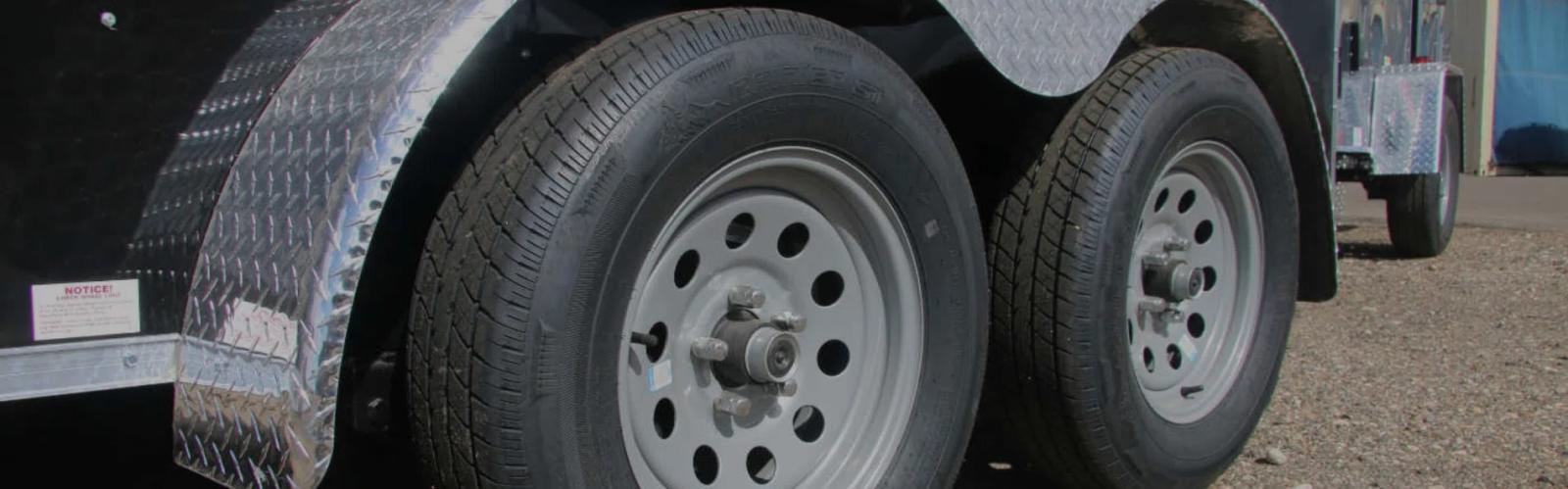 Close-up of a black trailer's tandem axles with silver wheels and a silver diamond-plate fender