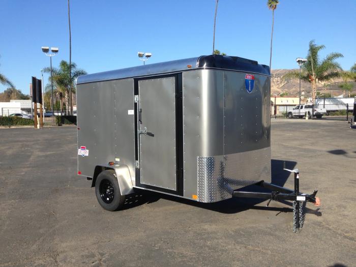 Silver Interstate Victory enclosed cargo trailer parked on asphalt with palm trees and mountains in the background