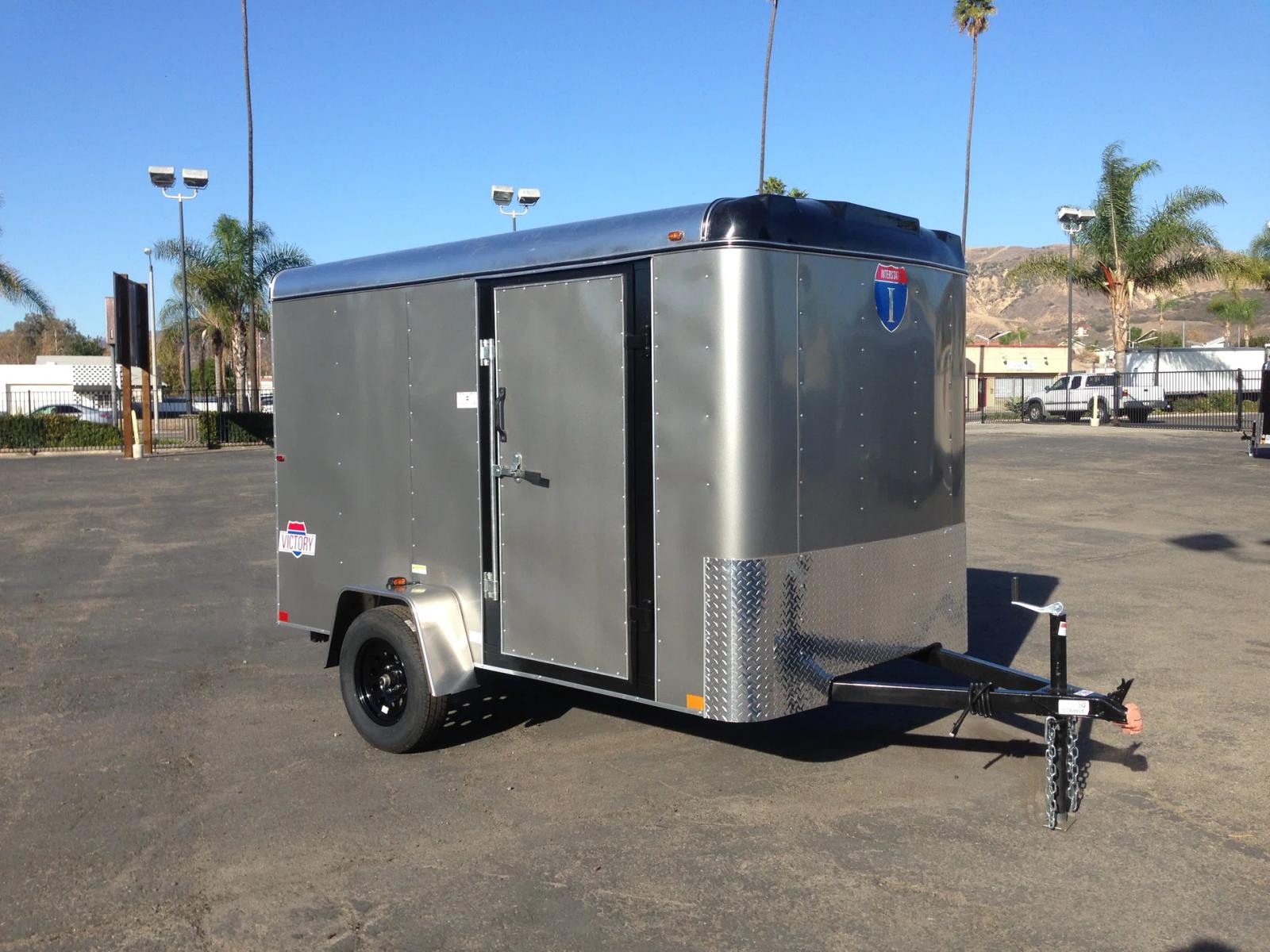 Silver Interstate Victory enclosed cargo trailer parked on asphalt with palm trees and mountains in the background