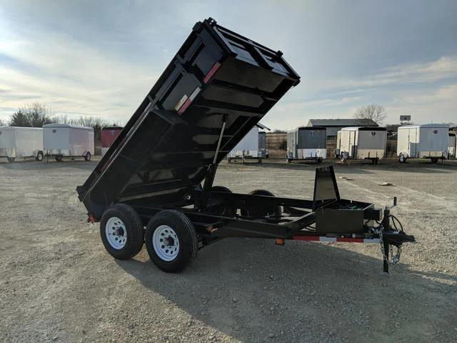 Black tandem-axle dump trailer with tall side extensions and bed tilted up in dump position, parked at a gravel dealer lot