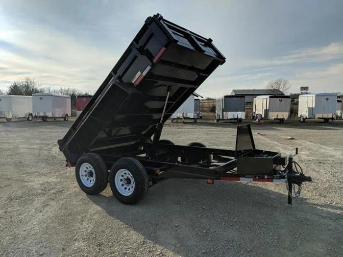 Three black dump trailers in varying sizes parked side-by-side on a sunny dirt lot ringed by trees