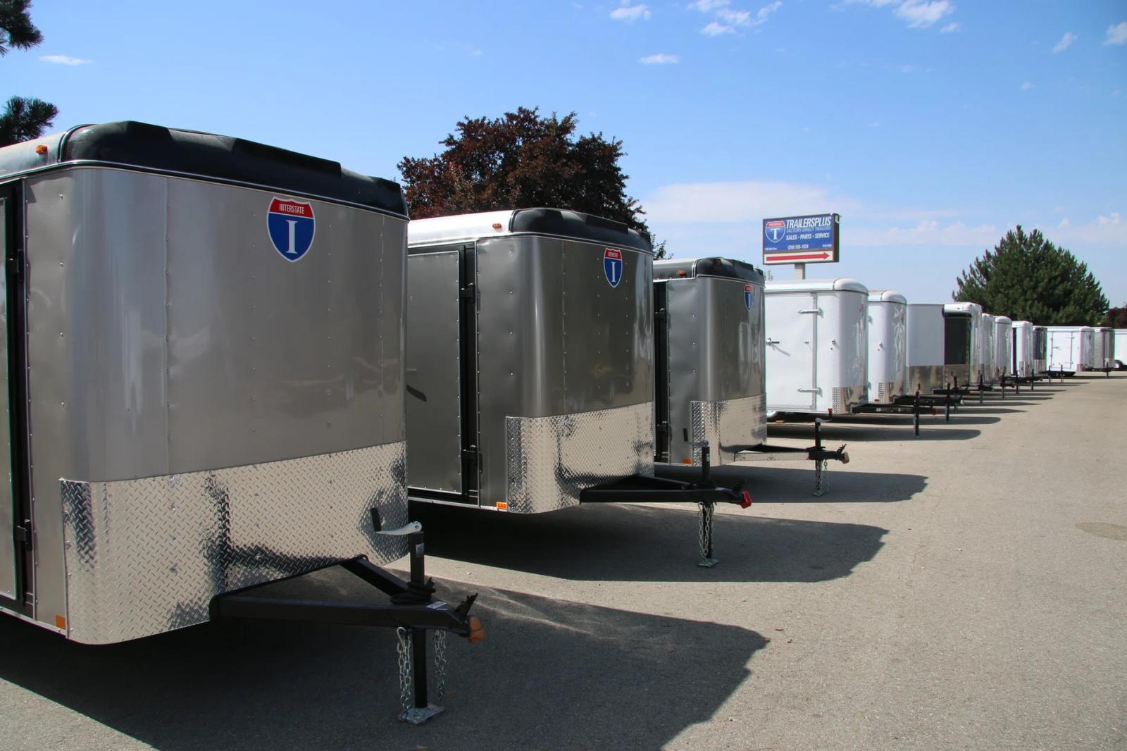 Side view of an Interstate Loadrunner enclosed cargo trailer with rear ramp deployed in front of a wood-framed house under construction