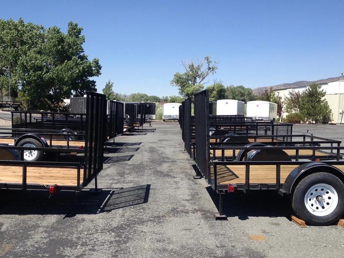Three black dump trailers of varying sizes parked side-by-side on a sandy dealer lot under a clear sky