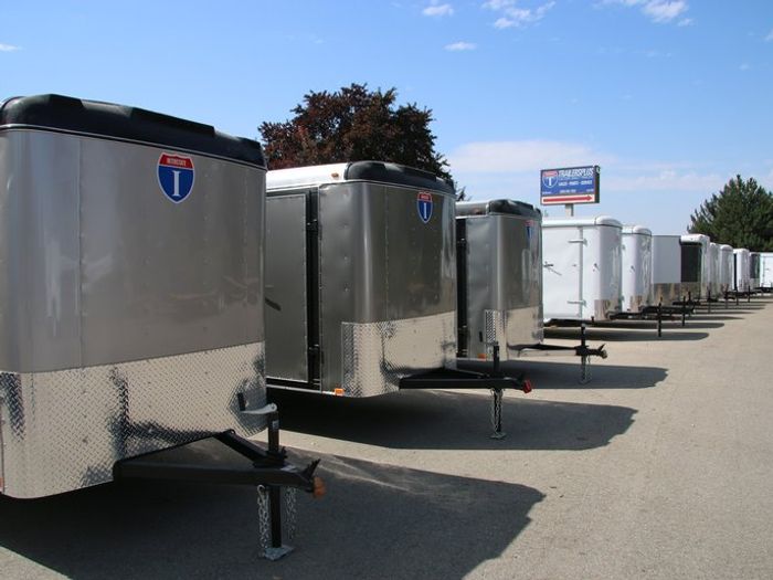 Side view of an Interstate Loadrunner enclosed cargo trailer with rear ramp deployed in front of a wood-framed house under construction