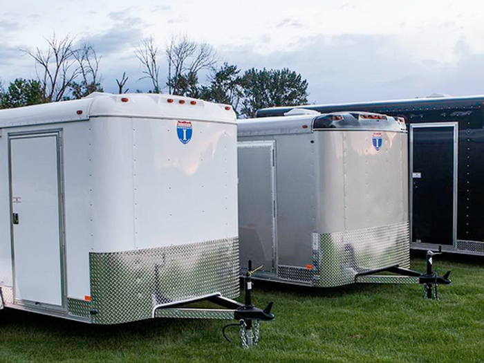 Charcoal-gray Interstate enclosed cargo trailer with diamond-plate stone guard parked on asphalt under a clear blue sky