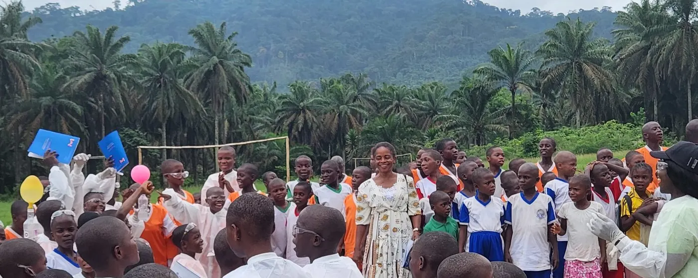 Pupils, teachers and parents gathered outdoors with forested hills behind them