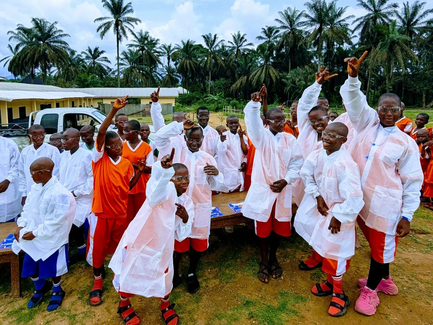 Pupils in white lab coats and safety glasses cheering with their hands raised