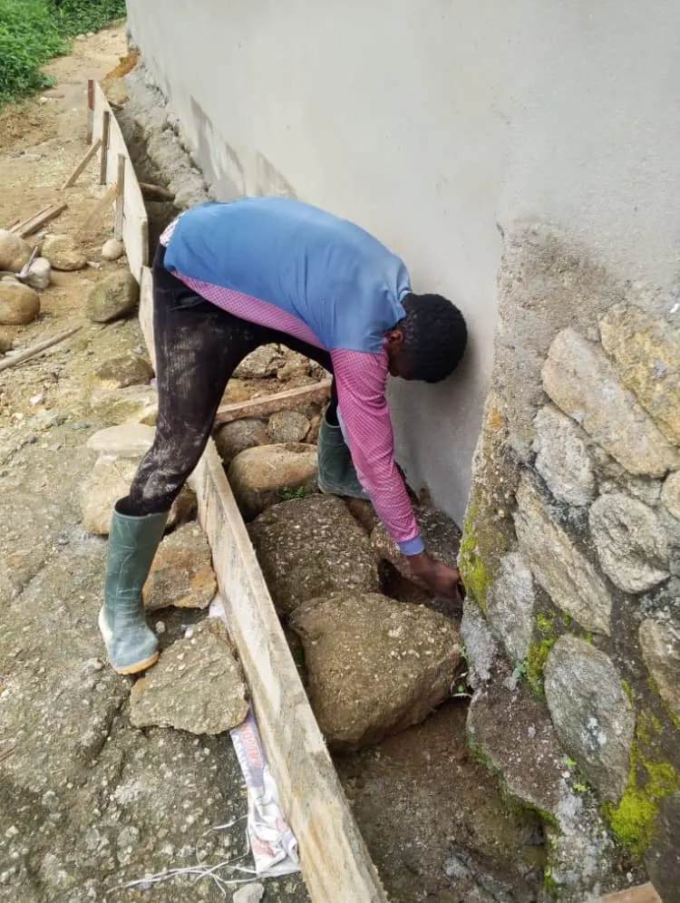 A builder setting large stones into the foundation along a freshly plastered wall