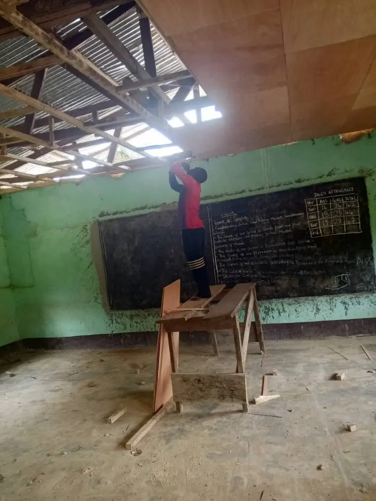 A worker standing on a desk fitting ceiling boards under the new roof