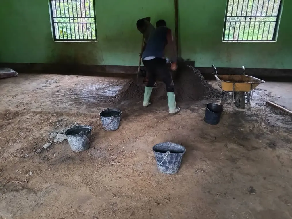 Two workers mixing concrete on the earth floor of a classroom