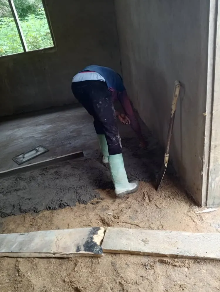 A builder spreading concrete across a classroom floor