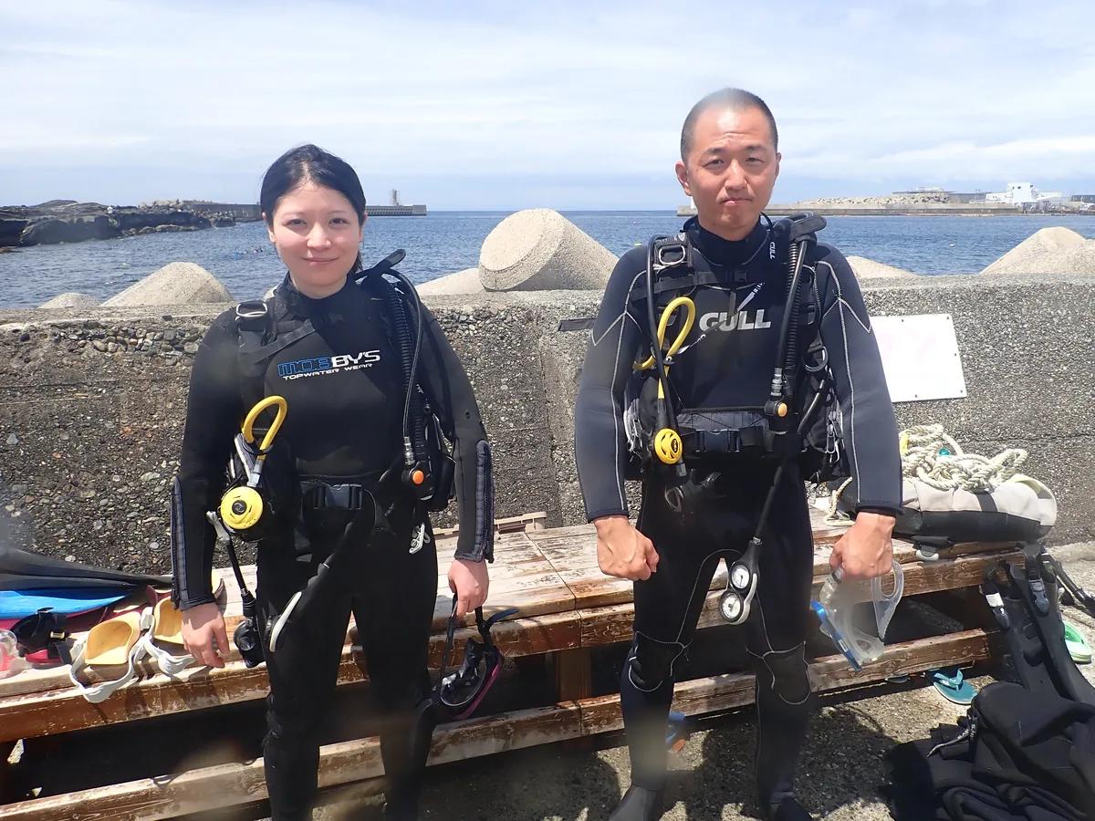 体験ダイビングの器材を背負い、エントリー前に城ヶ島の海をバックに立つお二人