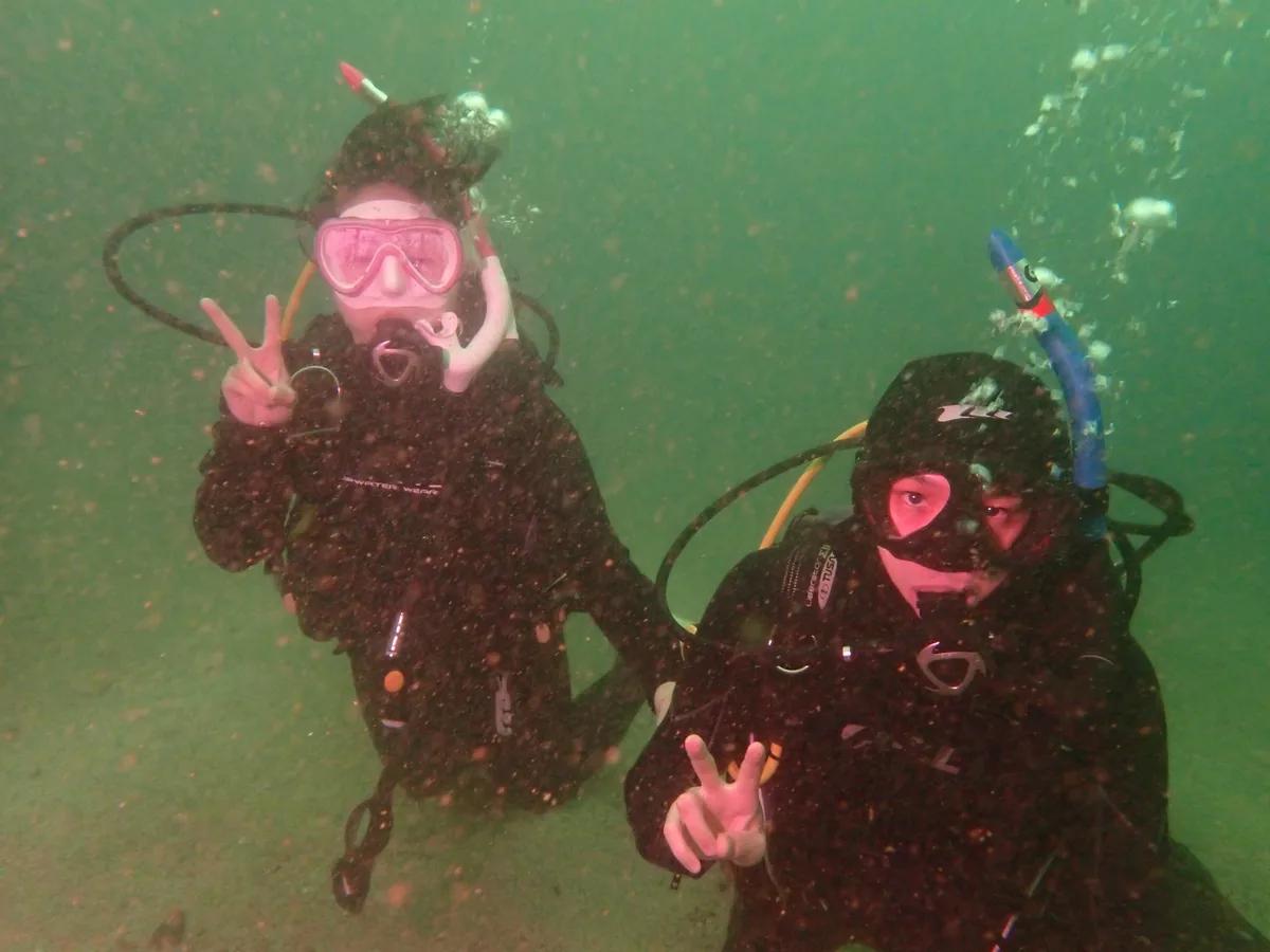 三浦の水中で並んでピースサインをするダイバーのご夫婦