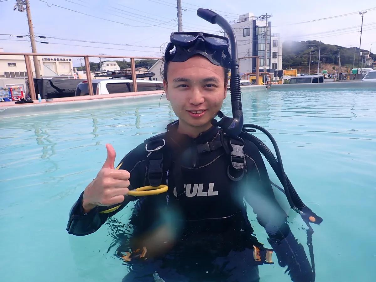 プールでダイビング器材を装着し、笑顔でOKサインを出す講習生