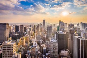 A breathtaking aerial view of New York City skyline at sunset, featuring the Empire State Building and numerous skyscrapers bathed in golden light.