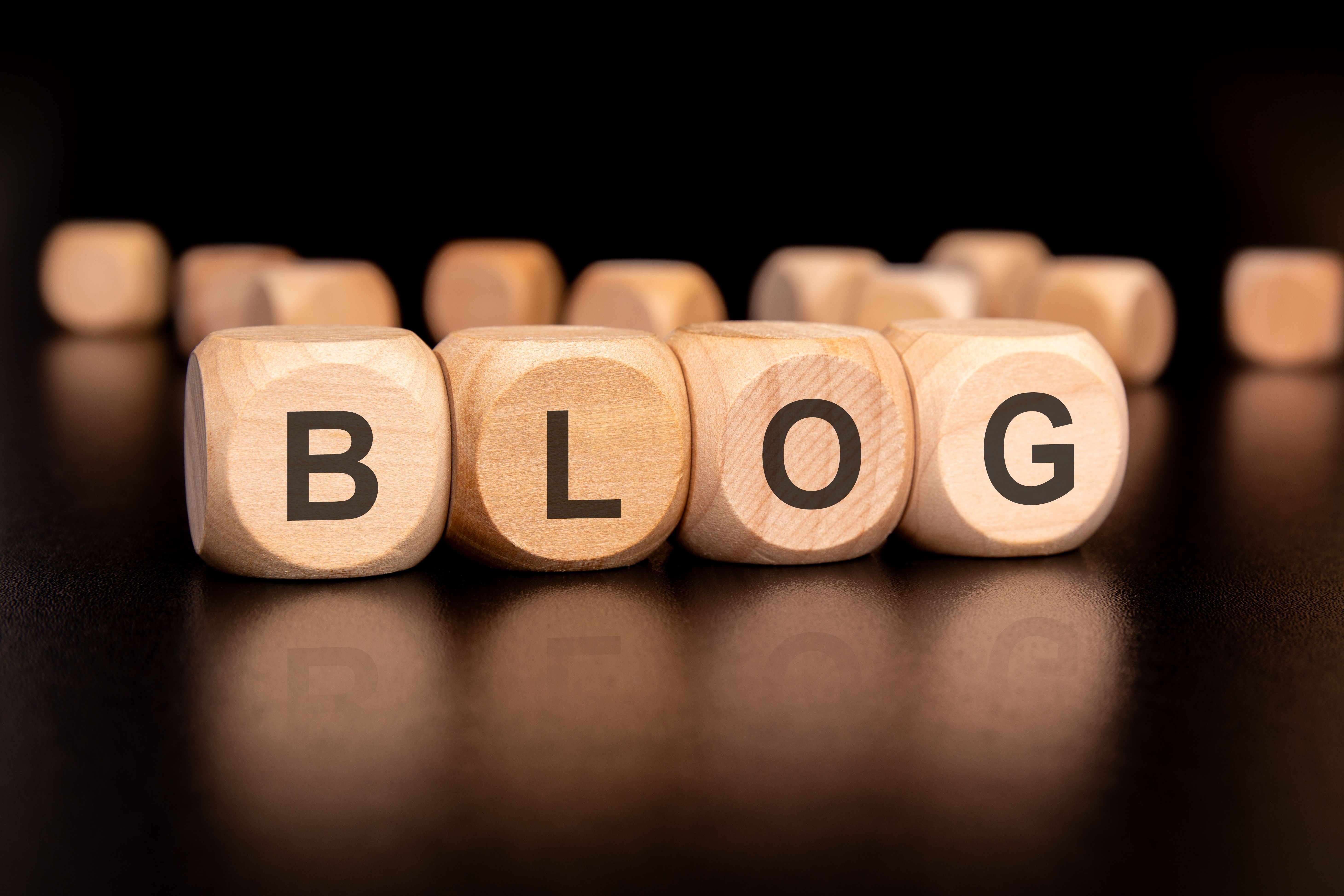 Wooden blocks spelling out the word 'BLOG' with other scattered blocks in the background, placed on a reflective black surface.