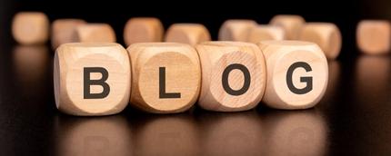 Wooden blocks spelling out the word 'BLOG' with other scattered blocks in the background, placed on a reflective black surface.