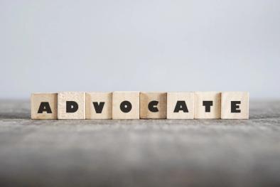 Wooden blocks spelling the word 'Advocate' arranged in a row on a neutral surface, symbolizing advocacy and support.