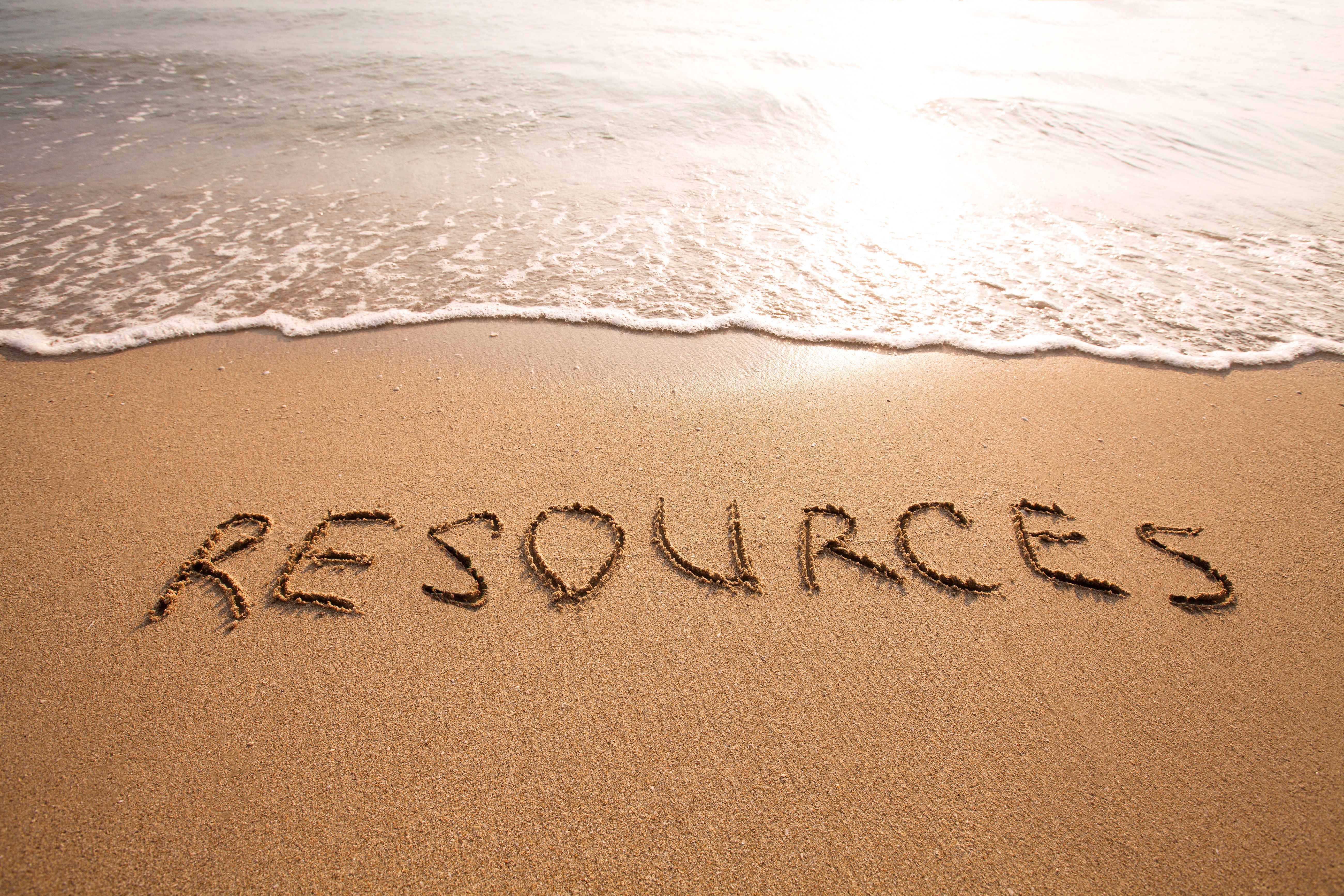 The word Resources written in the sand on a sunny beach with waves gently washing ashore in the background