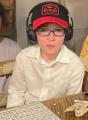 Halen, Tracie Smith's son, dressed in a white shirt, wearing a red and black cap and headphones, sitting at a table with a bingo card in front of him.