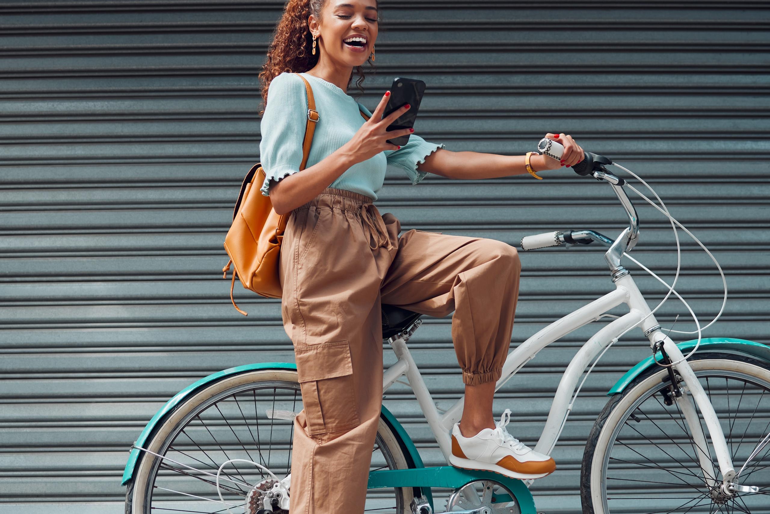 Young woman resting on her bicycle while checking her mobile phone and smiling