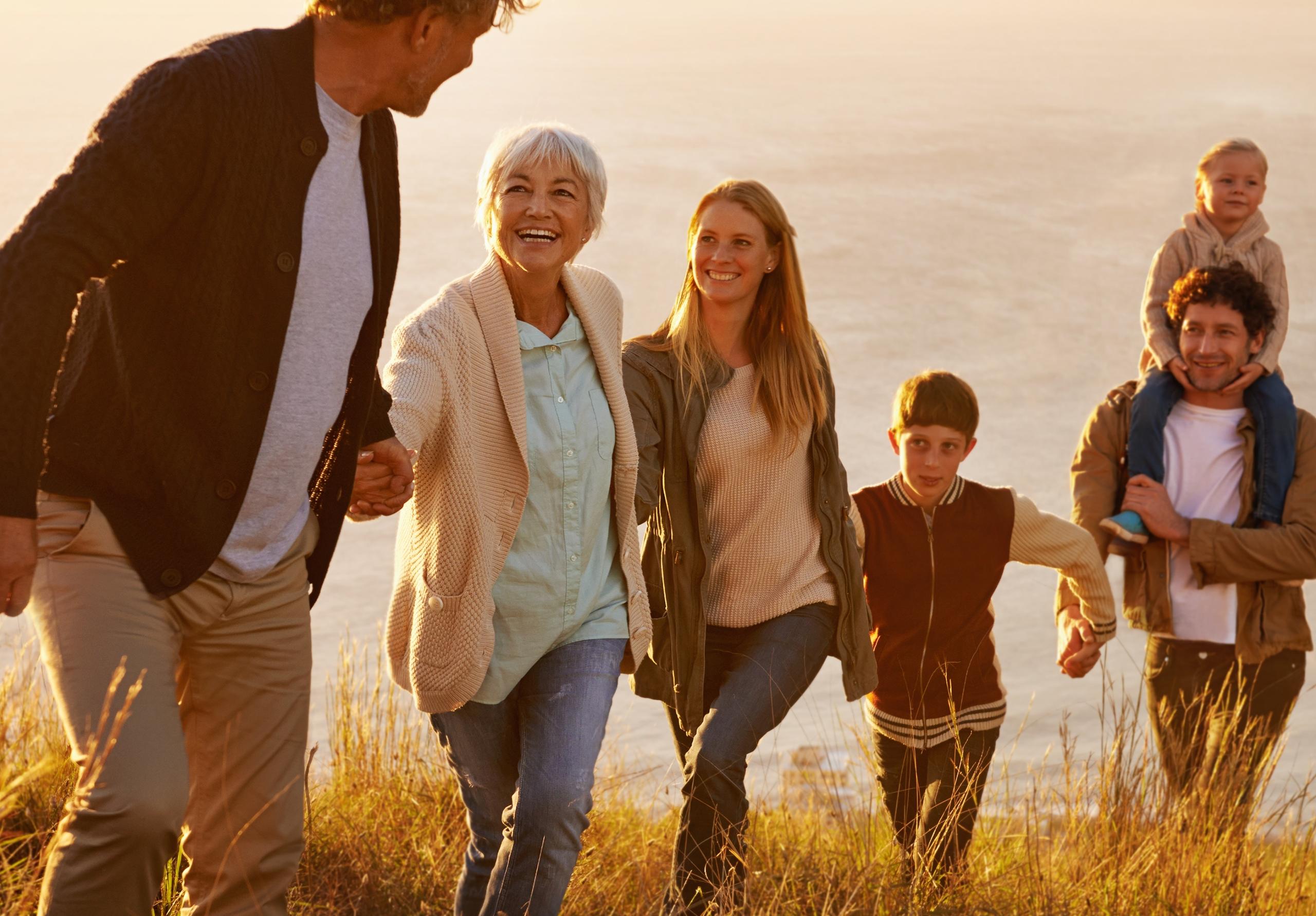 Family holding hands and walking through a field near the ocean in the late afternoon