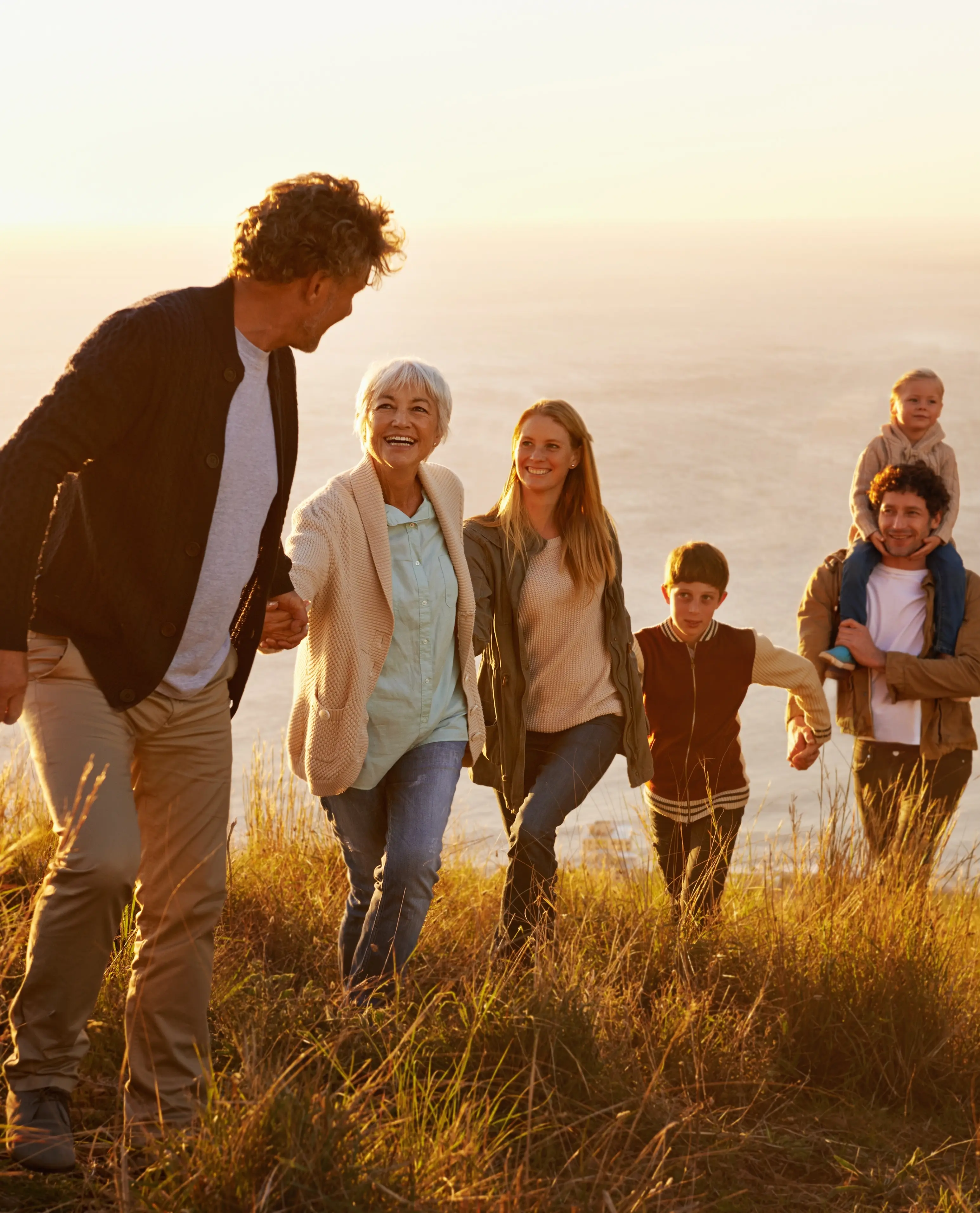 Family holding hands and walking through a field near the ocean in the late afternoon