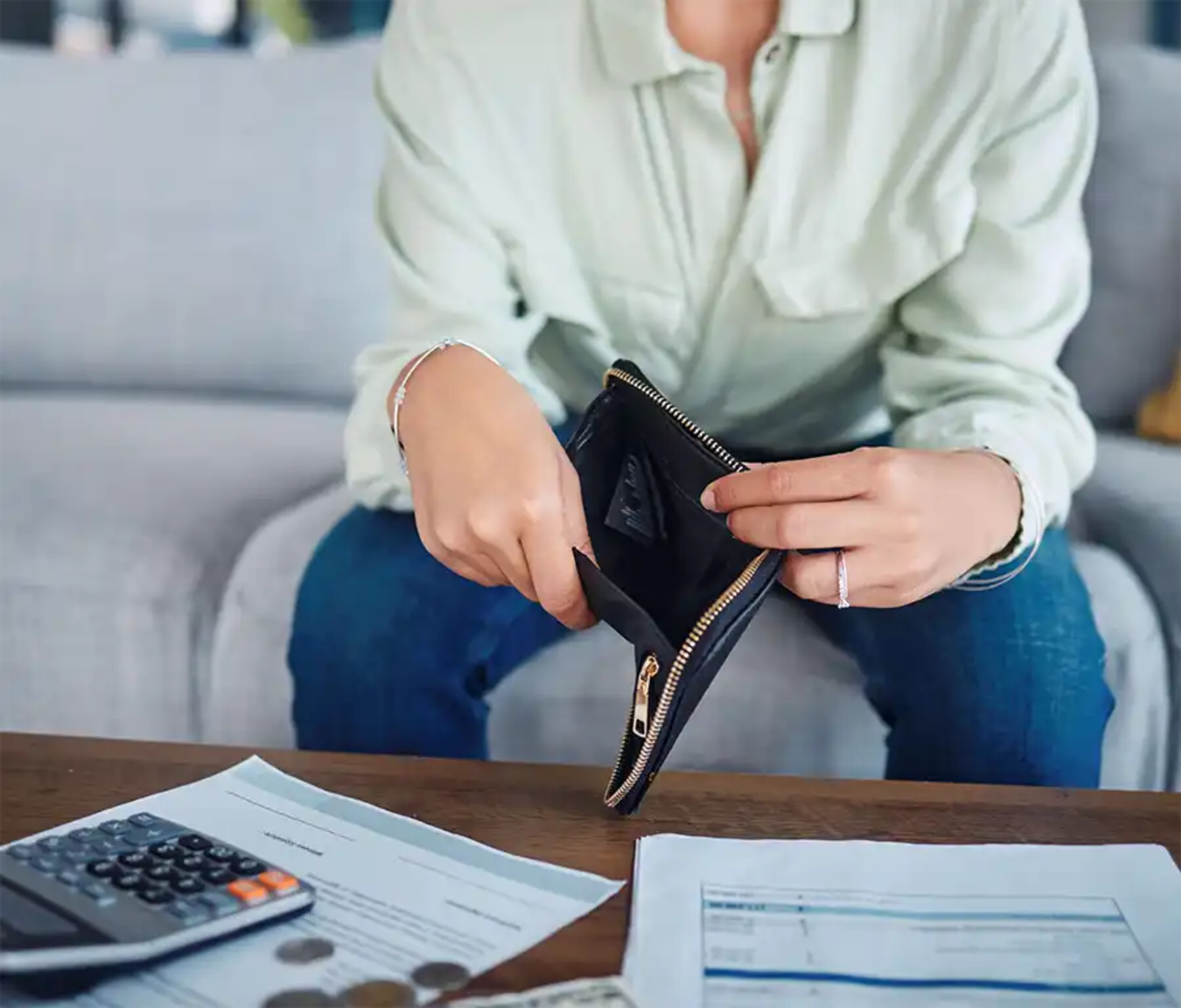 Woman with an empty purse with a calculator and bills on the table